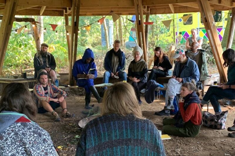 A picture of a group of people sat under a wooden structure in a circle at theSustainability Creative Lab in September 2020 at Wild Rumpus
